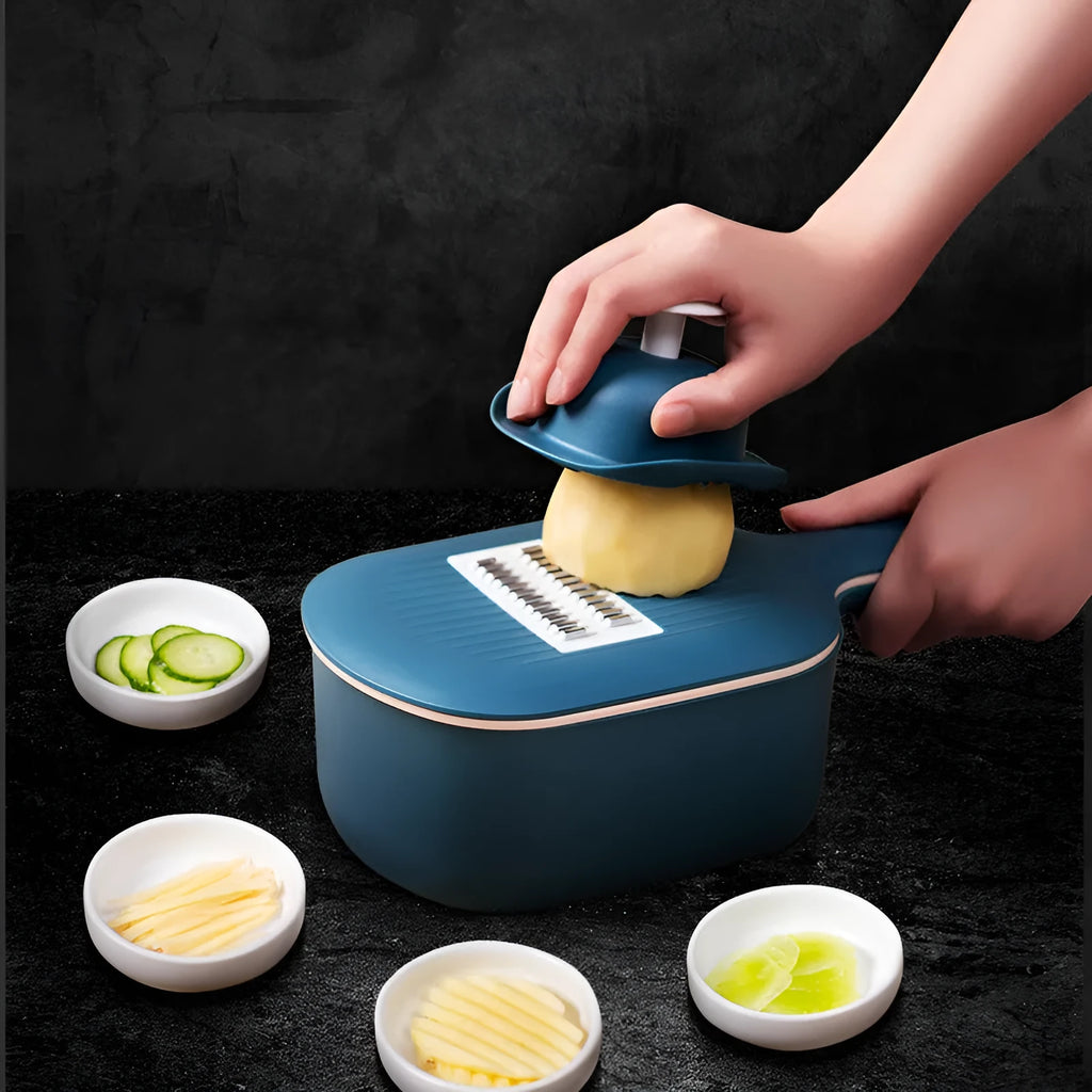 Dark blue vegetable cutter with four stainless steel blades, a drain basket, and a hand guard on a kitchen counter.