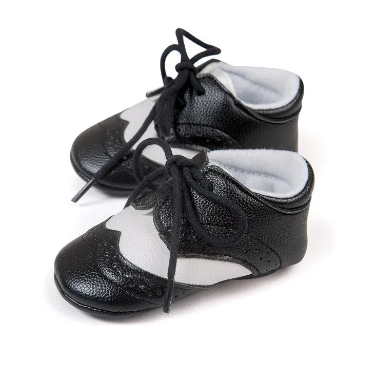 Vintage-style soft-soled baby shoes in black, grey, light brown, and white for infants 0-12 months.