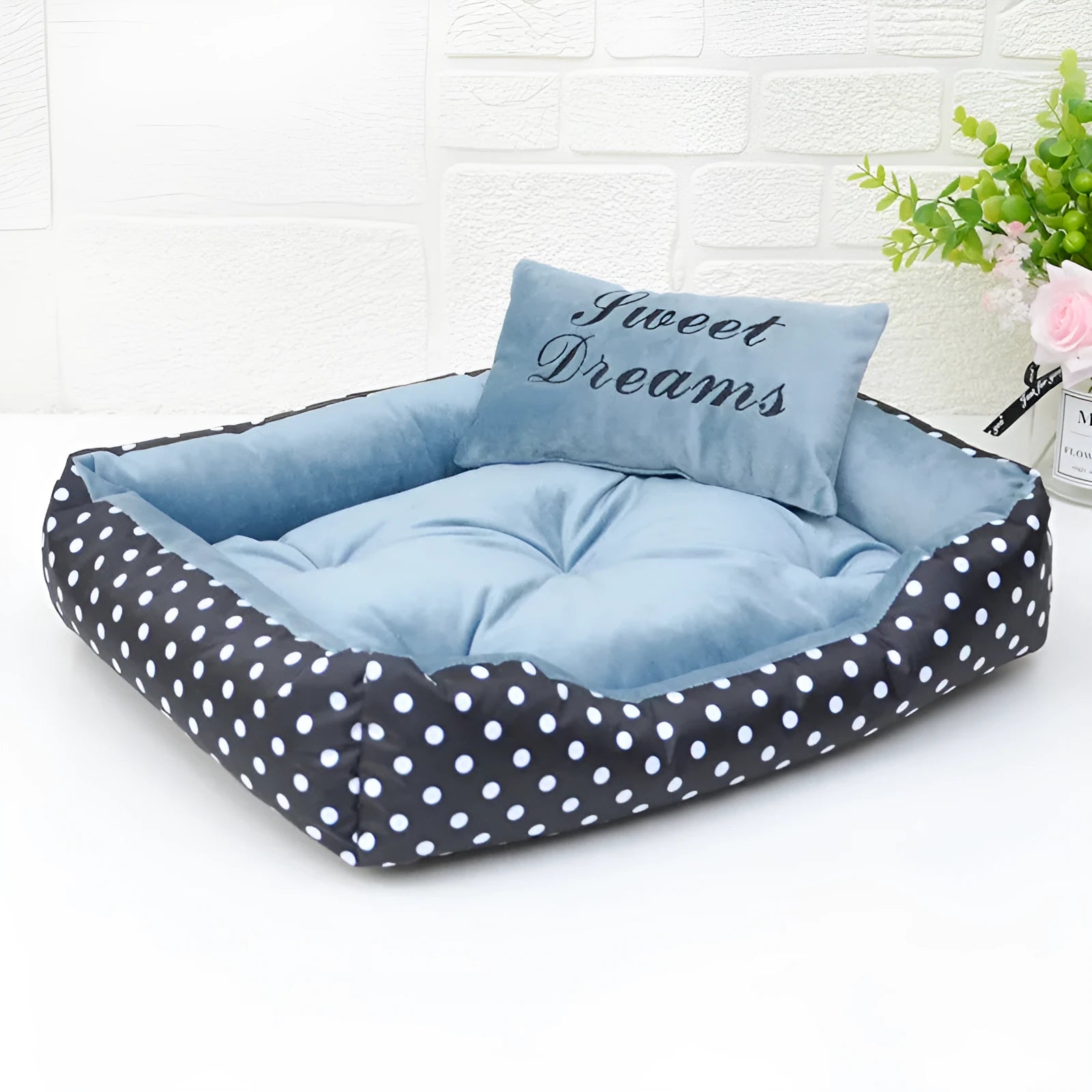 Polka dot square dog bed with matching embroidered pillow in grey, shown in a home setting.
