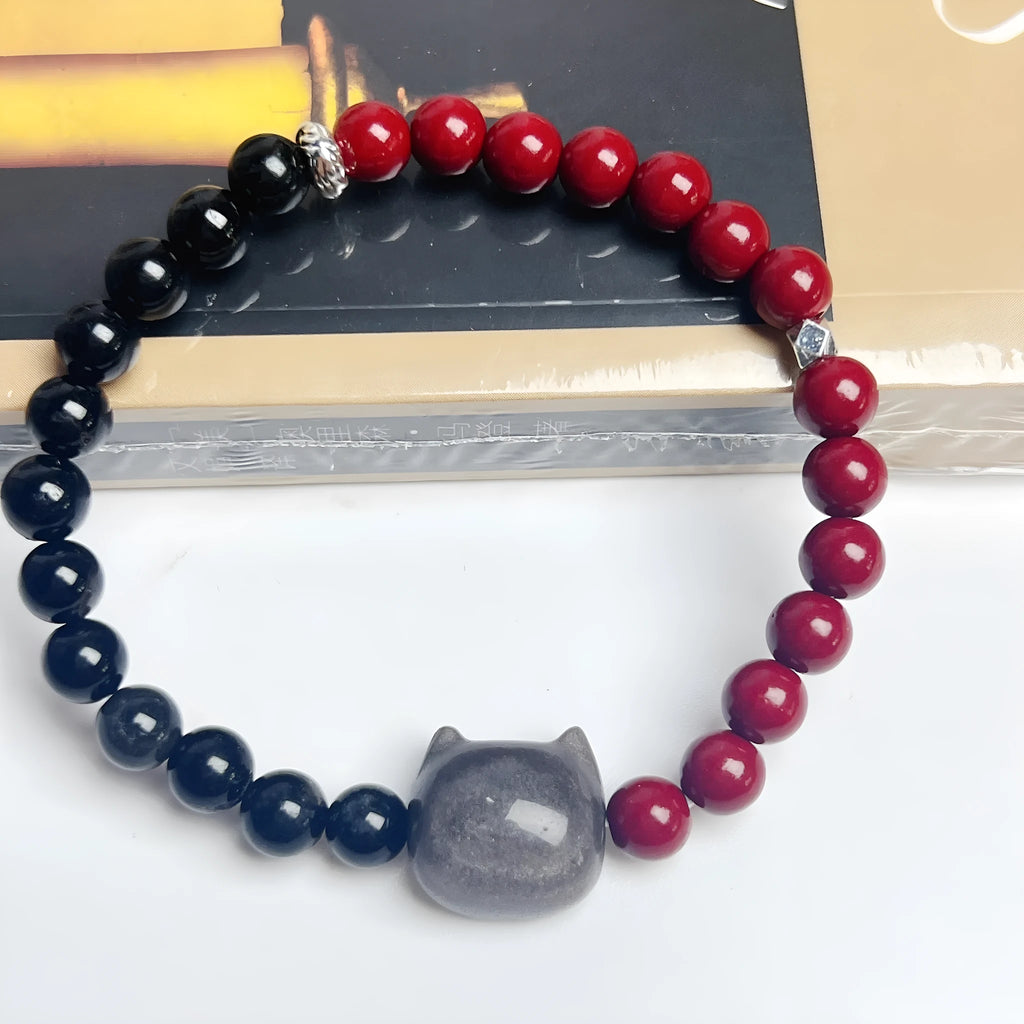 Black obsidian cat bracelet with golden crown charm and red bead on elastic cord