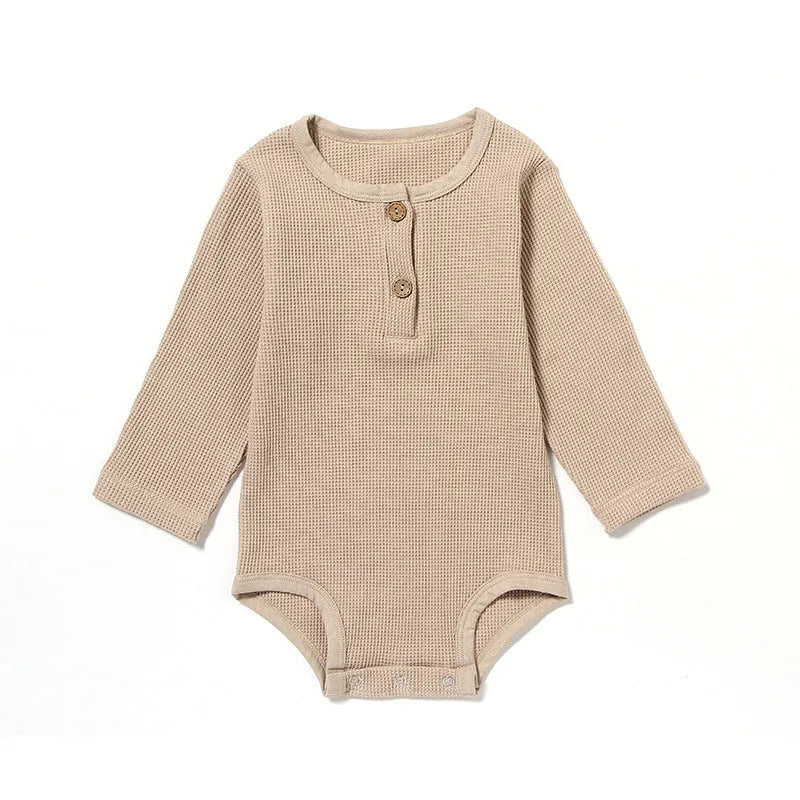 Long-sleeved waffle cotton baby romper in a neutral colour on a hanger, showing the triangular climbing front closure.
