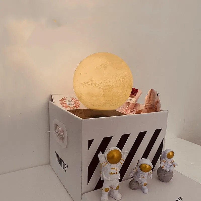 Moon planet floating LED night light with three astronaut figurines on dark surface