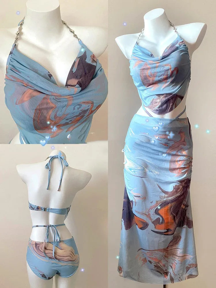 Women's blue printed bikini set with triangle top, bikini pants, and matching skirt laid flat.