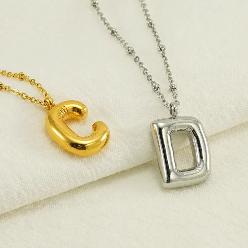 Gold bubble letter N pendant on stainless steel clip beads chain necklace against white background