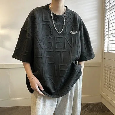 Men's grey loose-fit short sleeve t-shirt featuring a raised three-dimensional letter design on the front.