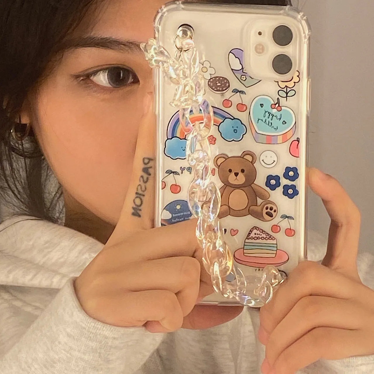 White iPhone case with a bear cartoon design and a silver chain with a bear pendant attached.