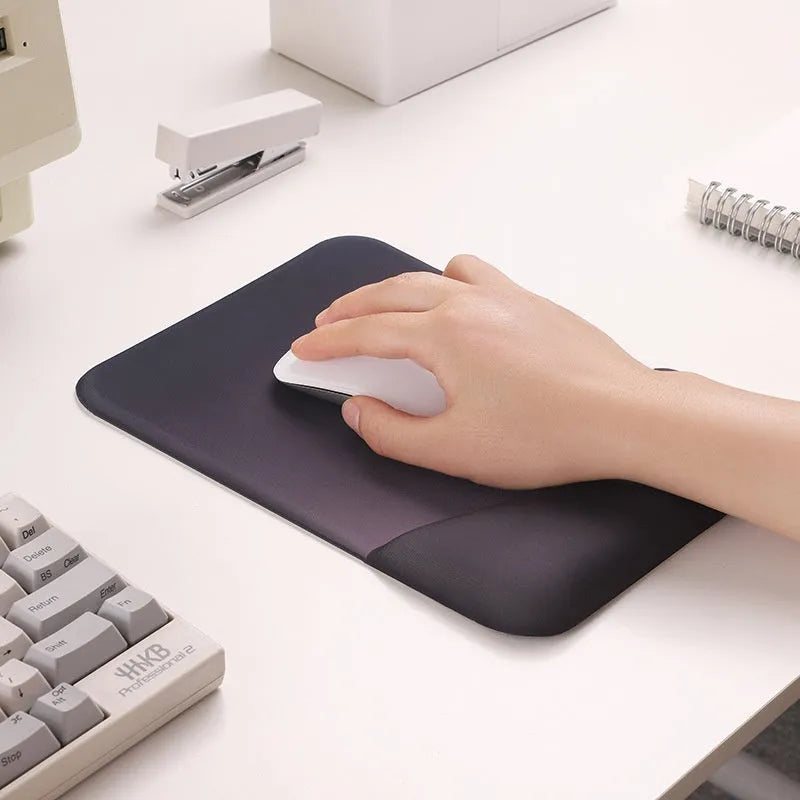 Square black silica gel wrist rest mouse pad on a desk, showing cloth surface and raised support pillow.