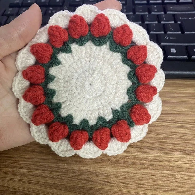 Set of four handmade woven floral coasters in pink, purple, red, and yellow on a wooden table.
