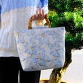Women's light blue canvas shoulder bag with bronzing flower detail showing horizontal square shape and double straps