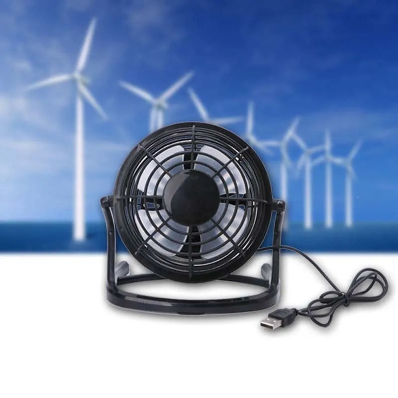 Small black USB desk fan with adjustable tilt on a wooden desk next to a laptop