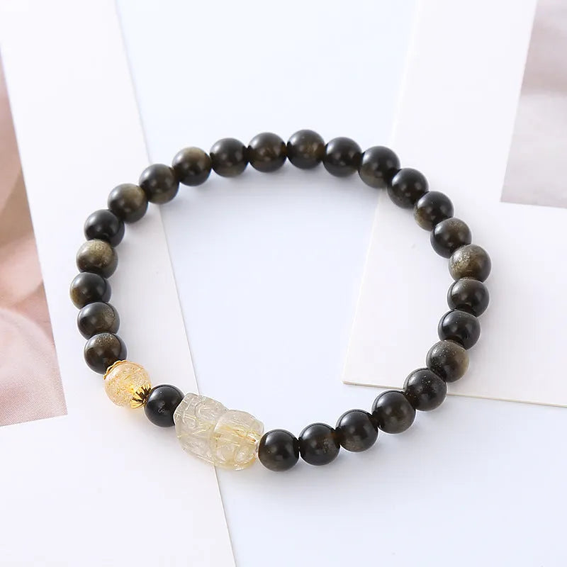 Handmade gold obsidian and red flower bead Pi Xiu bracelet on wrist, ethnic retro style.