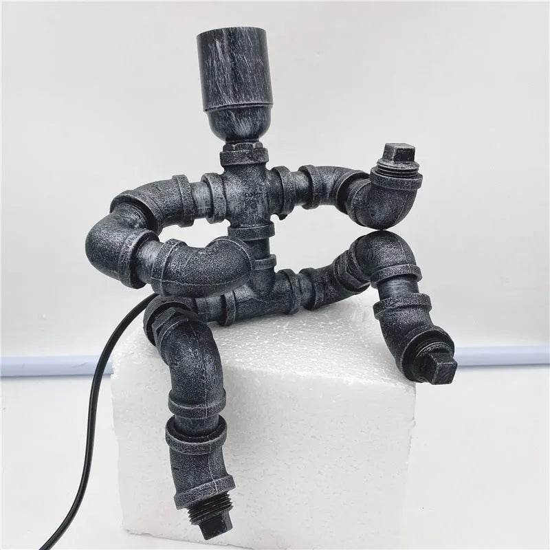 Custom industrial retro style iron pipe robot table lamp on a wooden desk.