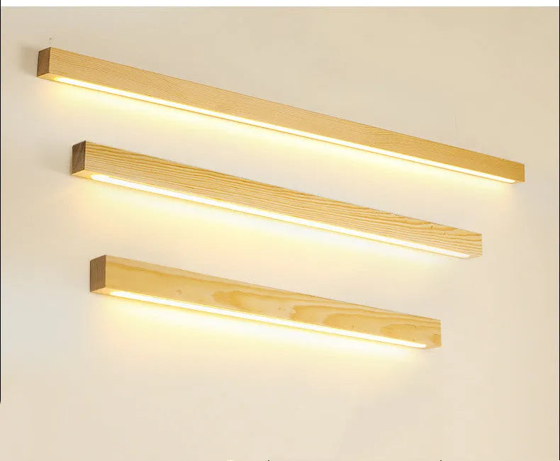 Long, slim walnut-coloured wooden wall lamp with integrated LED light, shown in a minimalist room setting.