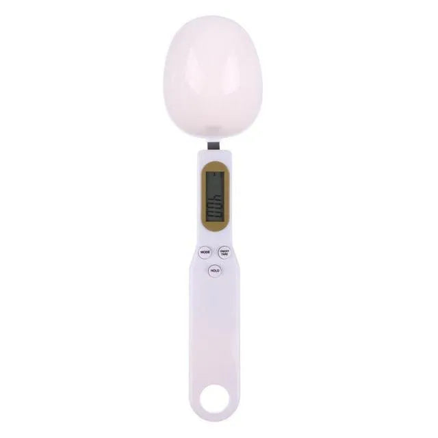 White digital kitchen scale with LCD screen displaying weight, shown next to a measuring spoon.