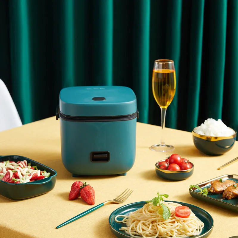 Green 1.2L mini rice cooker with metal body, steaming plate, rice spoon and measuring cup on countertop