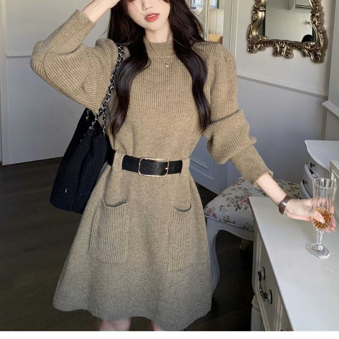 Women's long sleeve loose knitted dress in beige with a black belt, shown on a hanger.