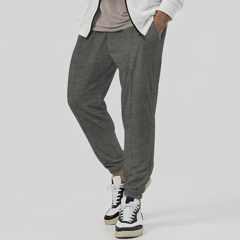 Man wearing grey loose tapered cotton blend track sweatpants with a straight leg.