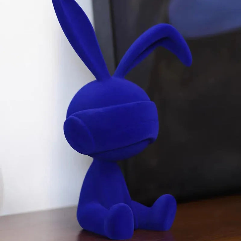 Green resin rabbit table ornament with suede blindfold on wooden surface
