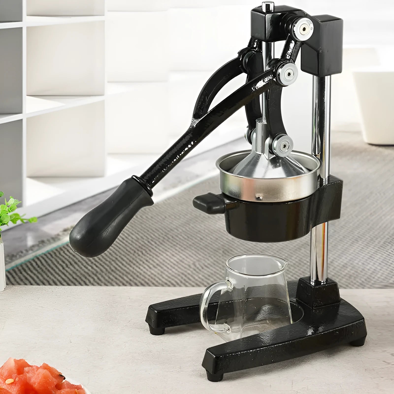 Black manual cast iron citrus juicer with stainless steel funnel on a kitchen counter.
