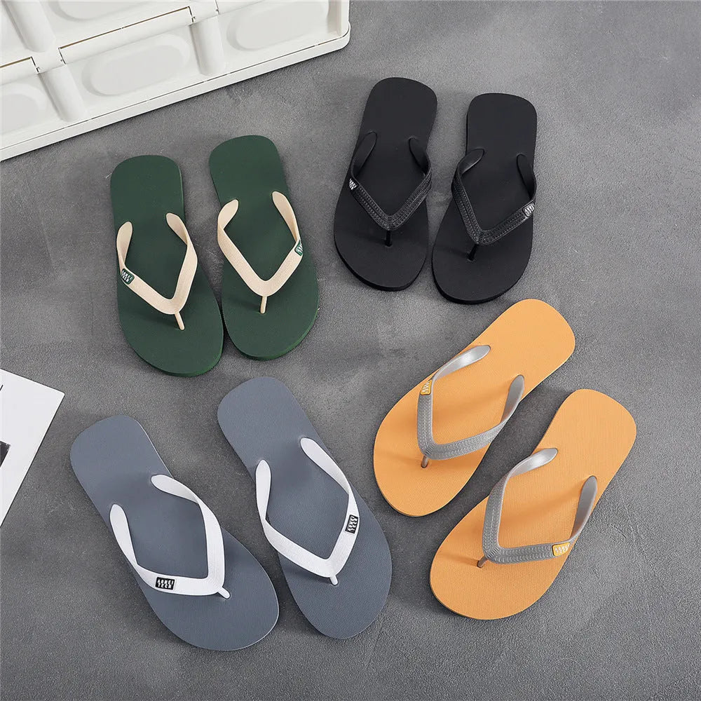 Men's black flip-flops with a textured rubber sole and EVA foam upper on a sandy beach.