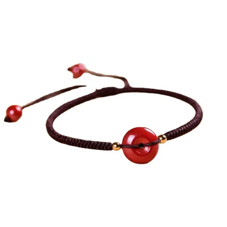 Traditional cinnabar bracelet with a heart-shaped peace buckle clasp on a red rope.