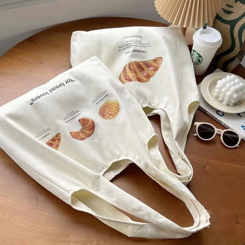 Beige canvas tote bag with bread print design showing adjustable shoulder strap and structured base