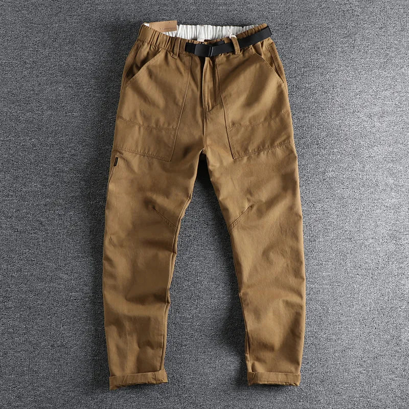 Man wearing khaki cotton work trousers with a buckle belt and structured three-dimensional cut.