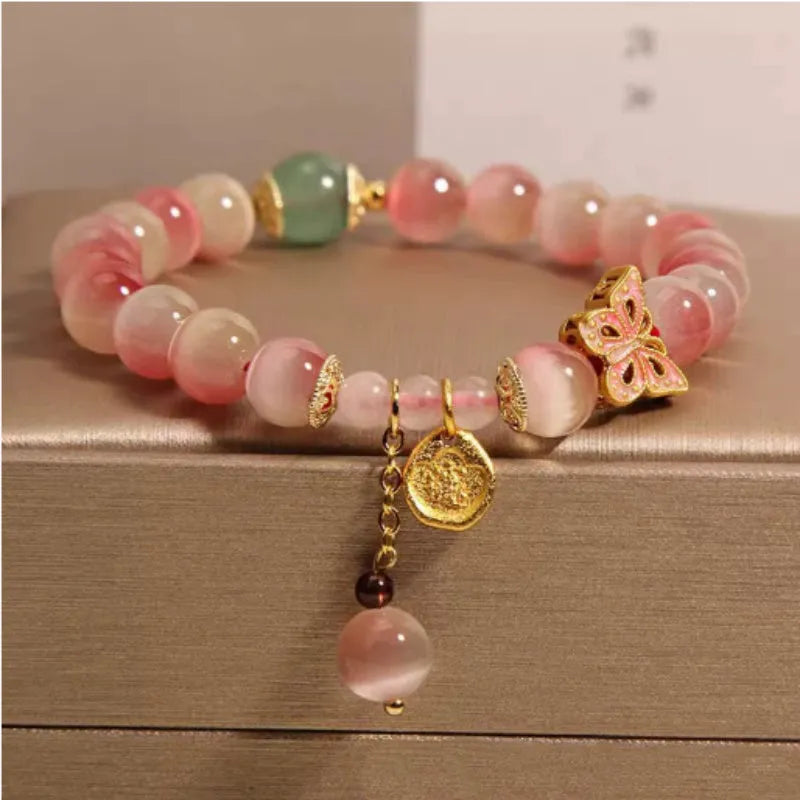 Close-up of a women's bracelet with a pink opal butterfly charm on an electroplated chain.
