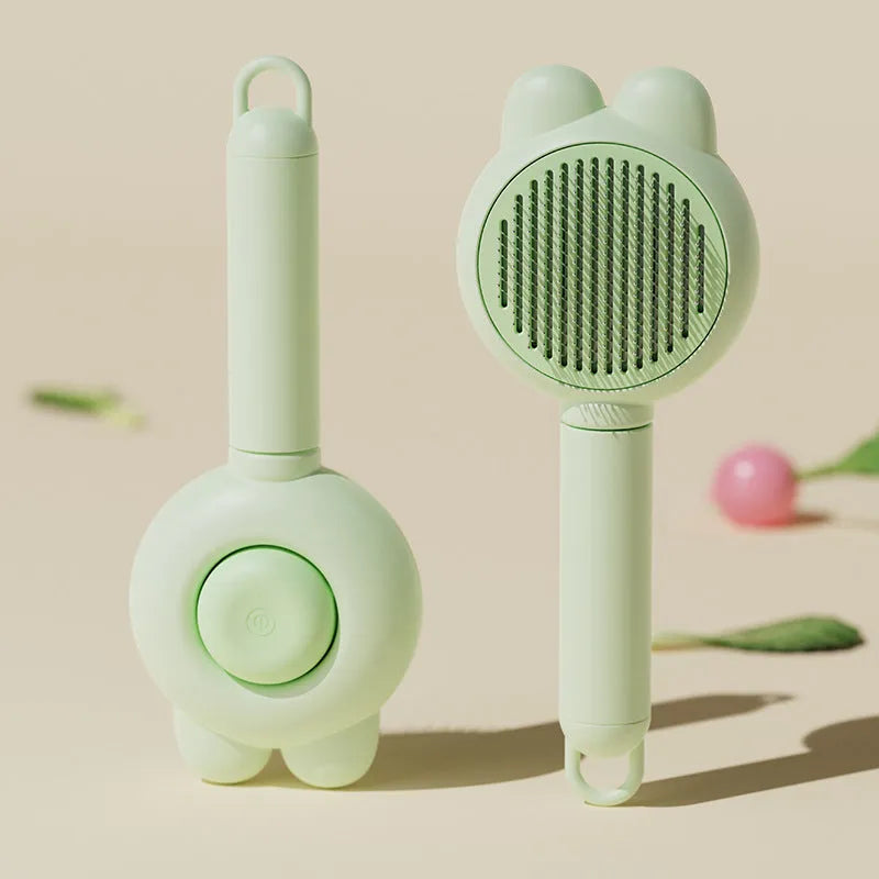 Green self-cleaning pet brush with a metal comb, release button, and comfort-grip handle for grooming cats and dogs.