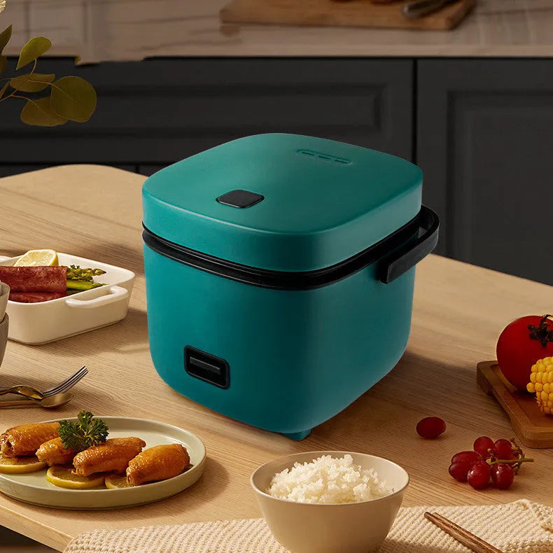 Green 1.2L mini rice cooker with metal body, steaming plate, rice spoon and measuring cup on countertop