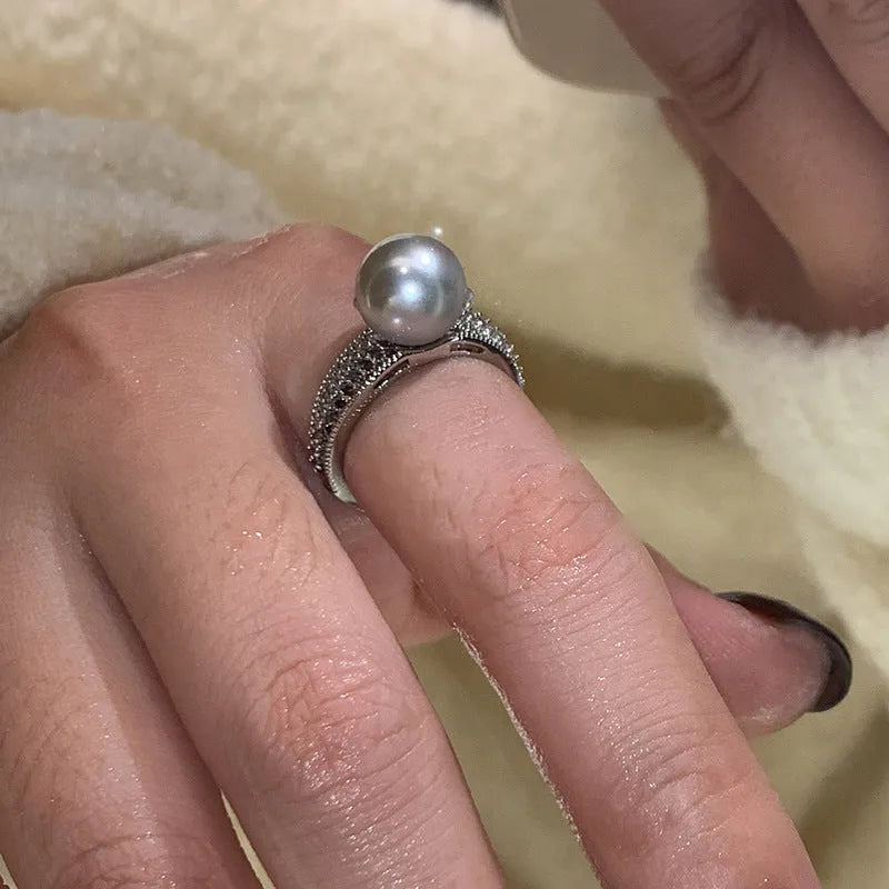 Adjustable open copper ring with a black pearl in a geometric shape for women, shown on an index finger.