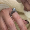 Adjustable open copper ring with a black pearl in a geometric shape for women, shown on an index finger.
