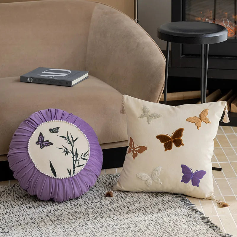 Square decorative cushion with Chinese butterfly embroidery in beige, black, and purple threads.