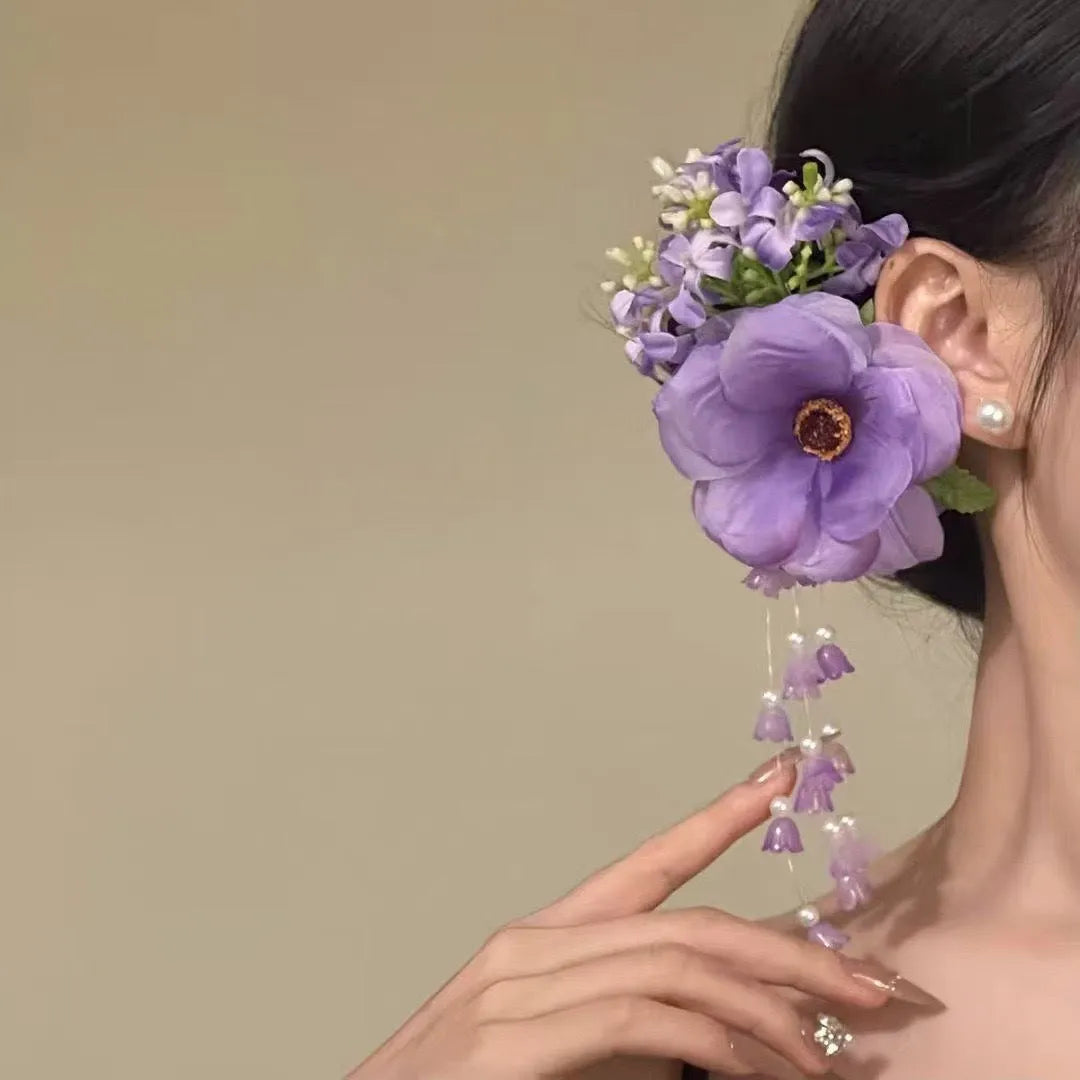 A handmade hair clip with a flower and tassel design in either yellow or purple.