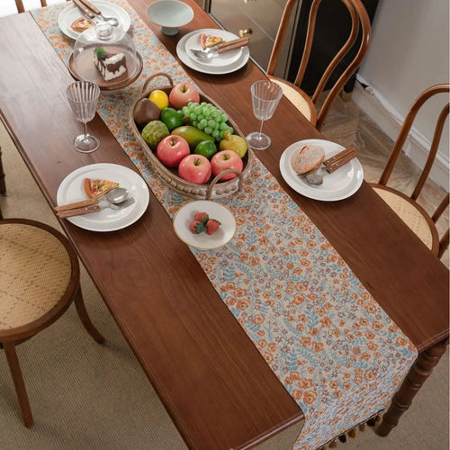 Beige jacquard fabric table runner with floral pattern and long tassels laid flat on a table.