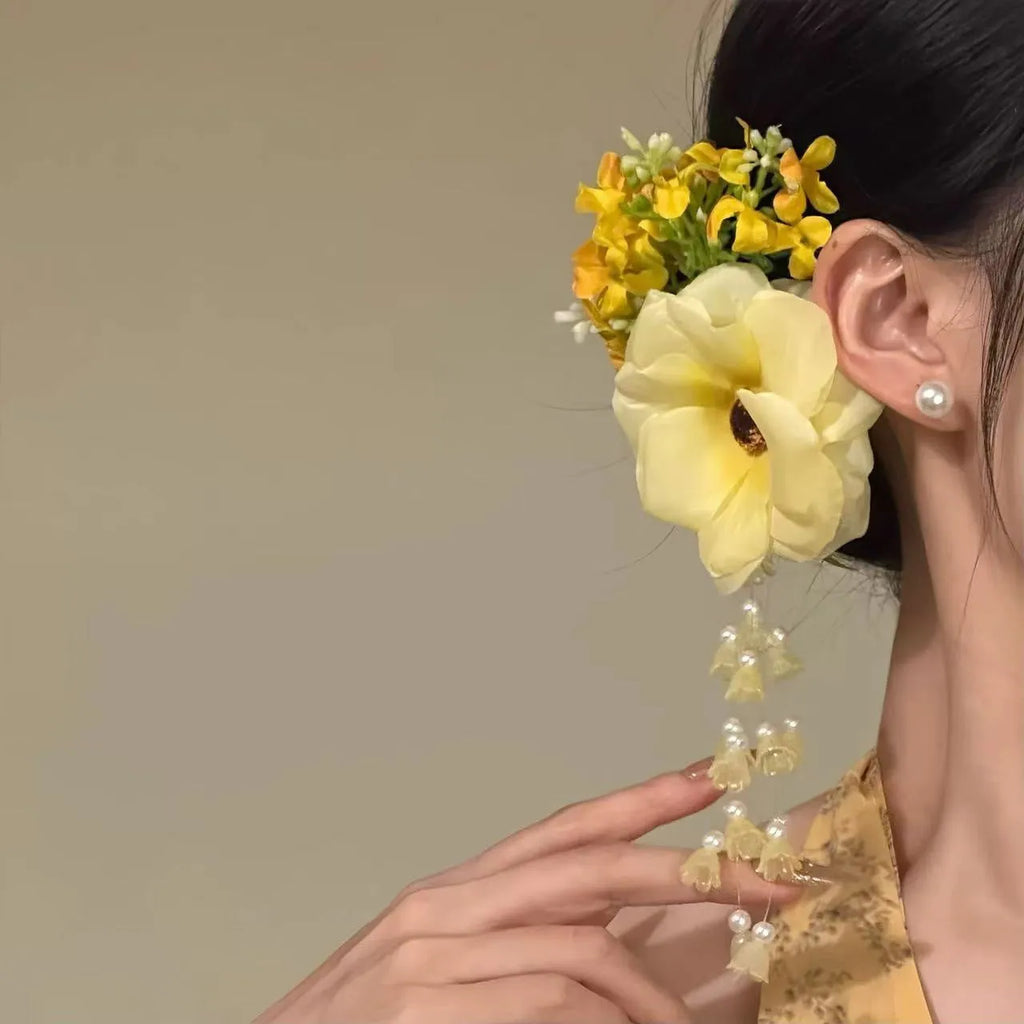 A handmade hair clip with a flower and tassel design in either yellow or purple.