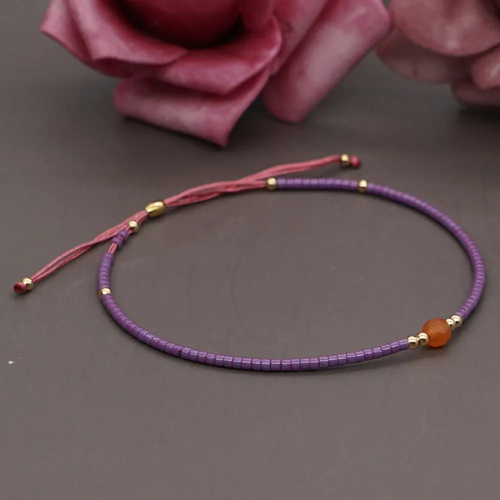 Close-up of a handmade women's bracelet with colourful glass and semi-precious stone geometric beads on a black stretch cord.