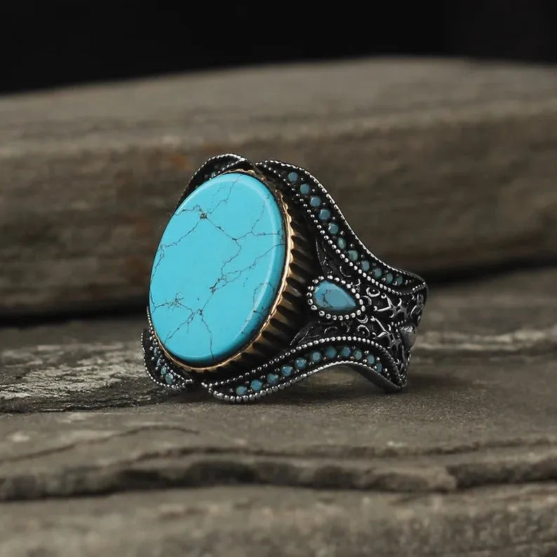 Men's round turquoise-style ring in antique silver alloy on a plain background.