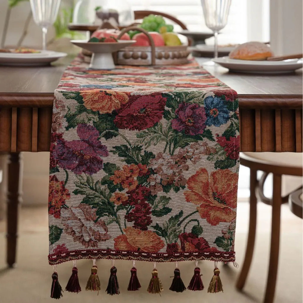 Beige jacquard fabric table runner with floral pattern and long tassels laid flat on a table.