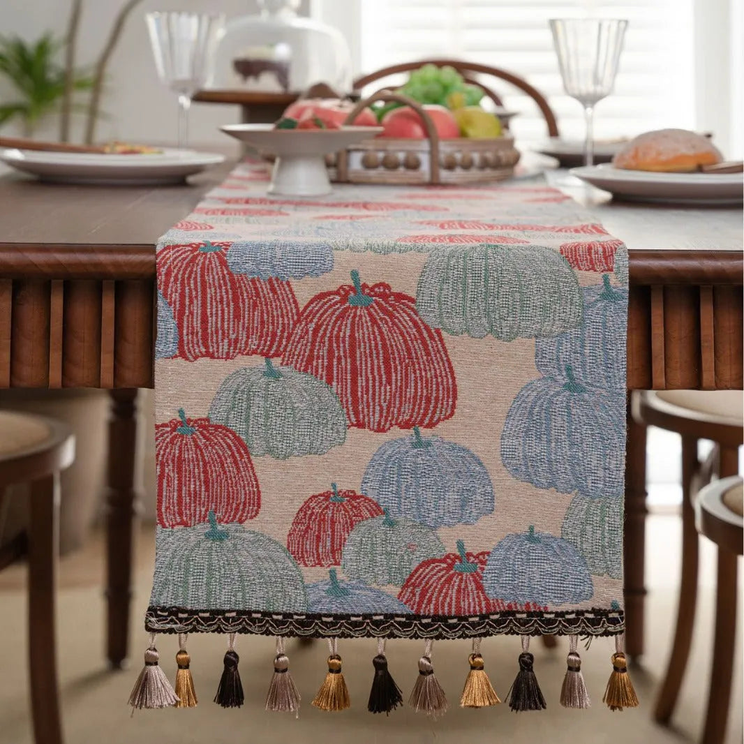 Beige jacquard fabric table runner with floral pattern and long tassels laid flat on a table.