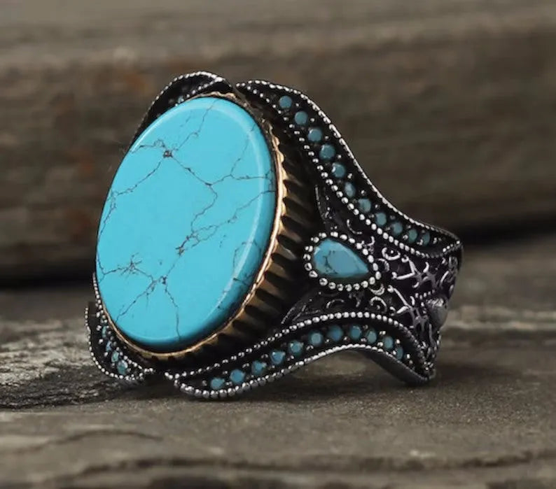 Men's round turquoise-style ring in antique silver alloy on a plain background.