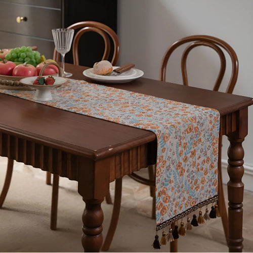 Beige jacquard fabric table runner with floral pattern and long tassels laid flat on a table.