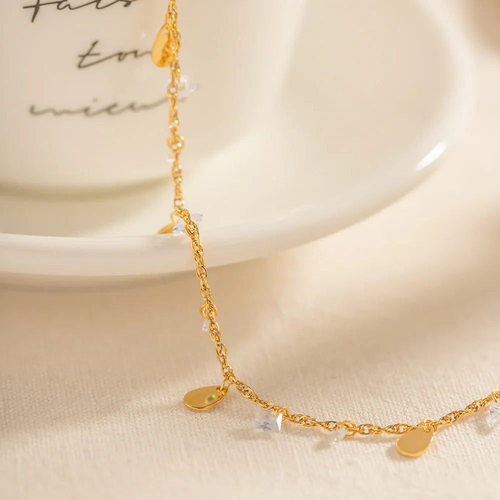 Stainless steel women's anklet with a geometric water drop tassel charm on an ankle.