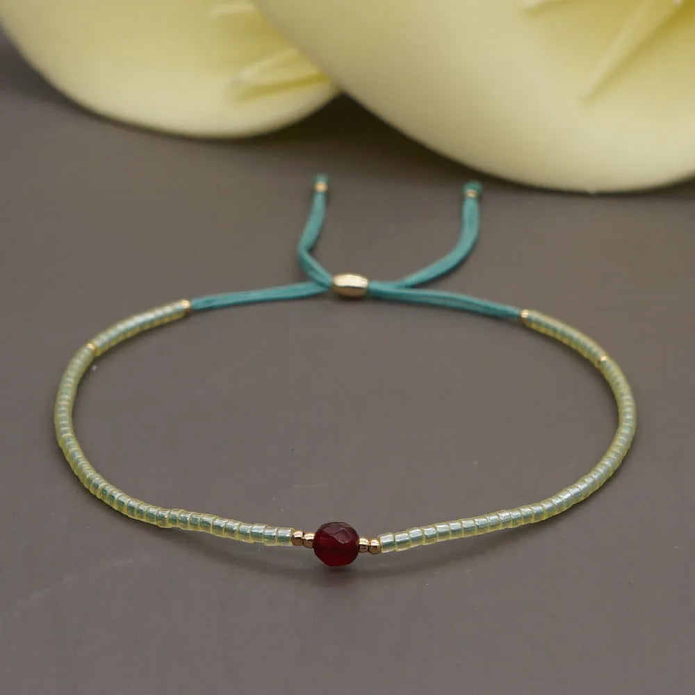 Close-up of a handmade women's bracelet with colourful glass and semi-precious stone geometric beads on a black stretch cord.