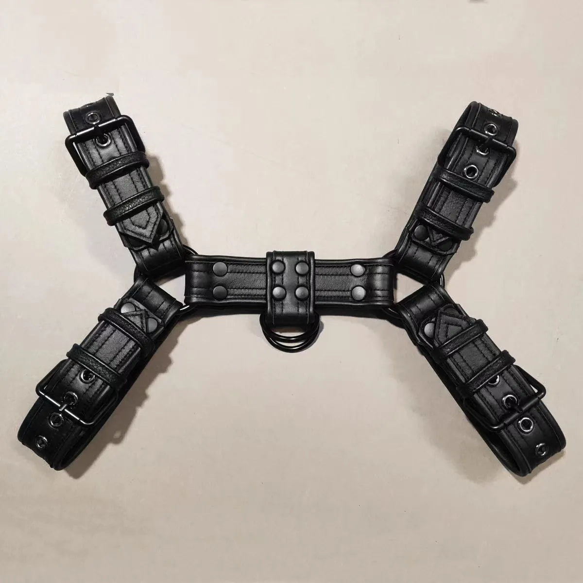 Black leather chest muscle bondage strap with metal buckle and rivets laid flat.