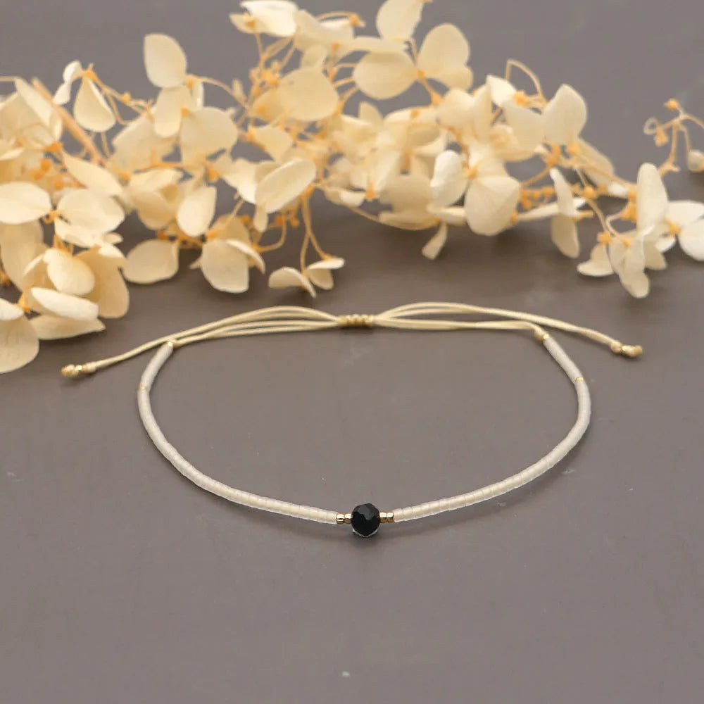 Close-up of a handmade women's bracelet with colourful glass and semi-precious stone geometric beads on a black stretch cord.