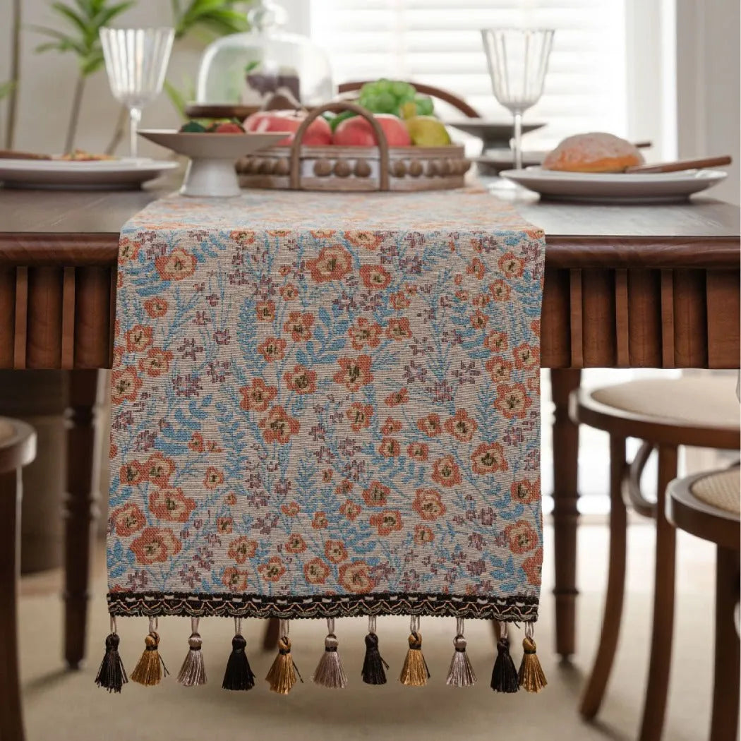 Beige jacquard fabric table runner with floral pattern and long tassels laid flat on a table.