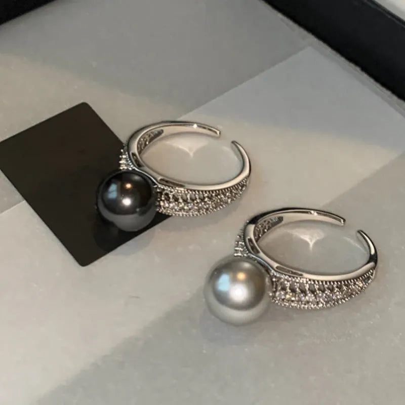 Adjustable open copper ring with a black pearl in a geometric shape for women, shown on an index finger.