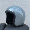 A retro-style grey half helmet for motorcycle riding, shown on a stand.