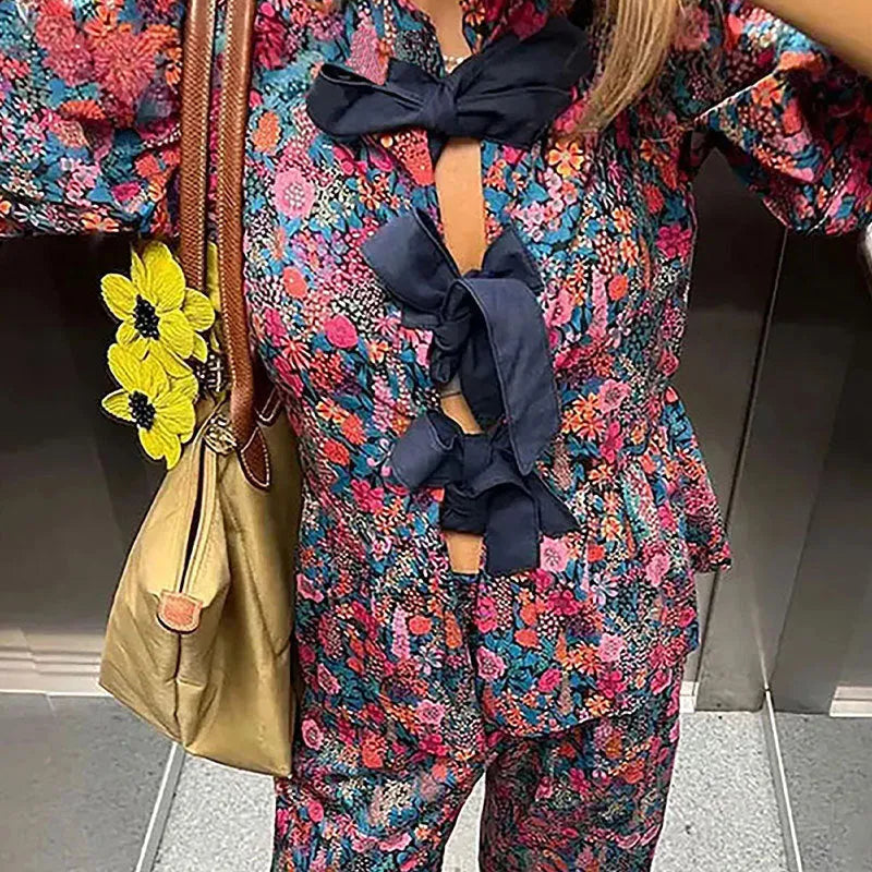 Women's floral print polyester trouser suit with tie-neck top and puff sleeves.